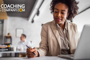 Affirmative writing shown by Person in office at desk writing goals with laptop