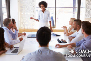 Coach doing Team Coaching in office with team members sat around desk