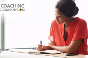 Leader journaling at desk wearing orange shirt