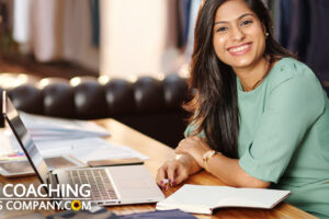 East Indian Coach at desk with laptop, pen and paper writing down successes