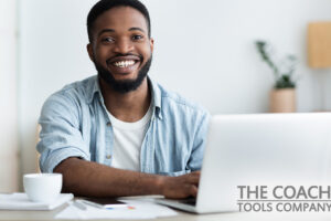 Happy Black male coach with Life Coaching Exercises sat at desk with a Laptop