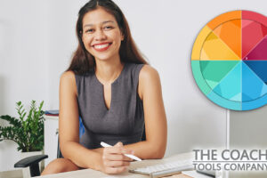 Coach at desk smiling and holding pen with Blank Colourful Coaching Wheel over the image