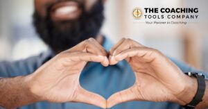 Smiling man holding his hands in a heart shape, symbolising kindness and compassion in coaching.