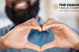 Smiling man holding his hands in a heart shape, symbolising kindness and compassion in coaching.